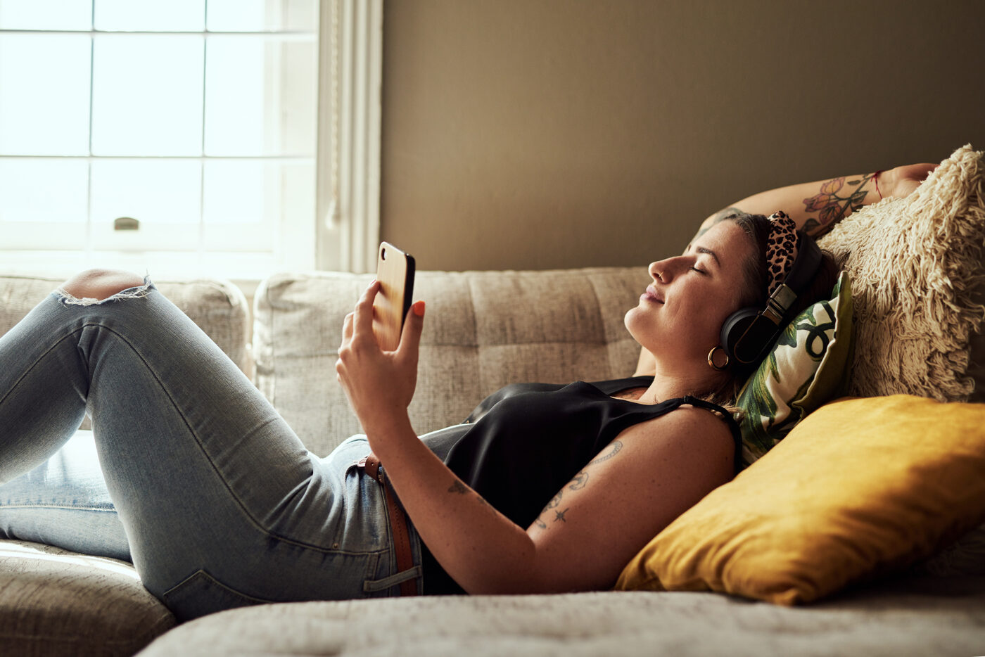 Frau liegt auf einem Sofa und schaut auf ihr Handy