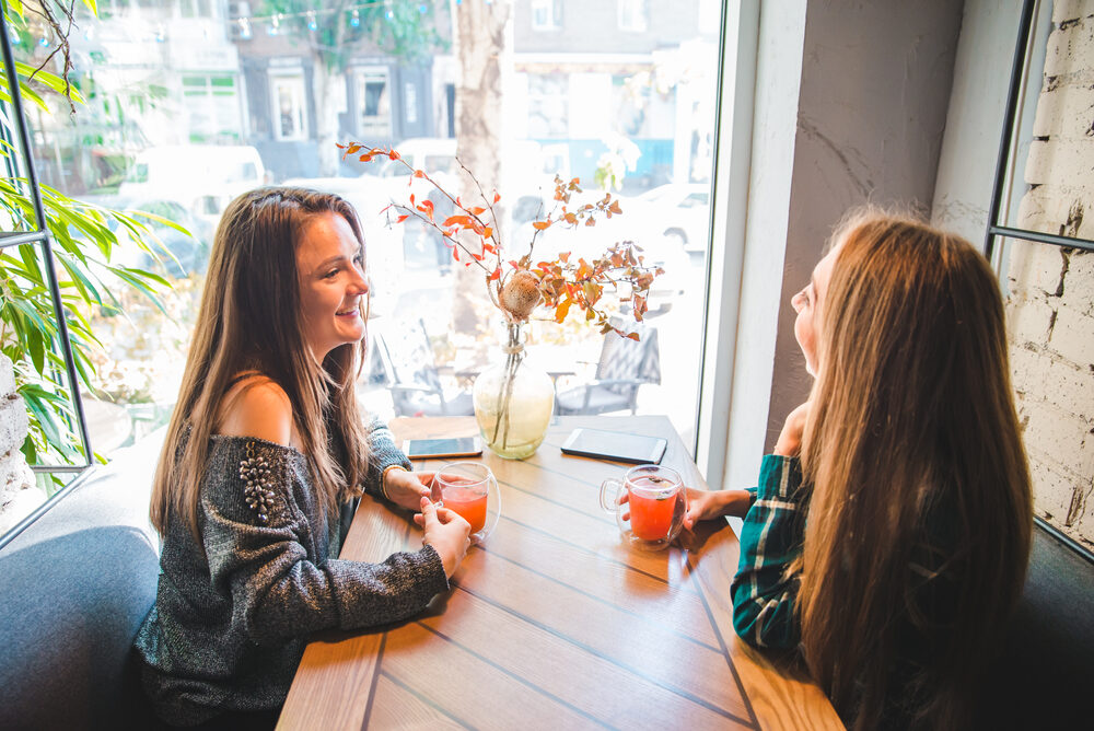 Zwei Frauen sitzen an einem Fenstertisch und unterhalten sich